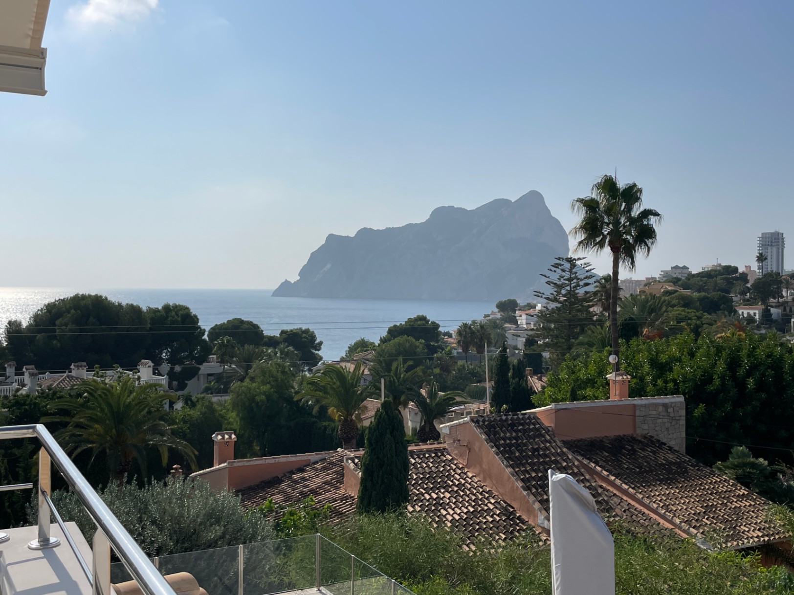 Vista panorámica al Peñón de Ifach y al Mediterráneo desde una terraza con barandilla de acero inoxidable y cristal, rodeada de vegetación.