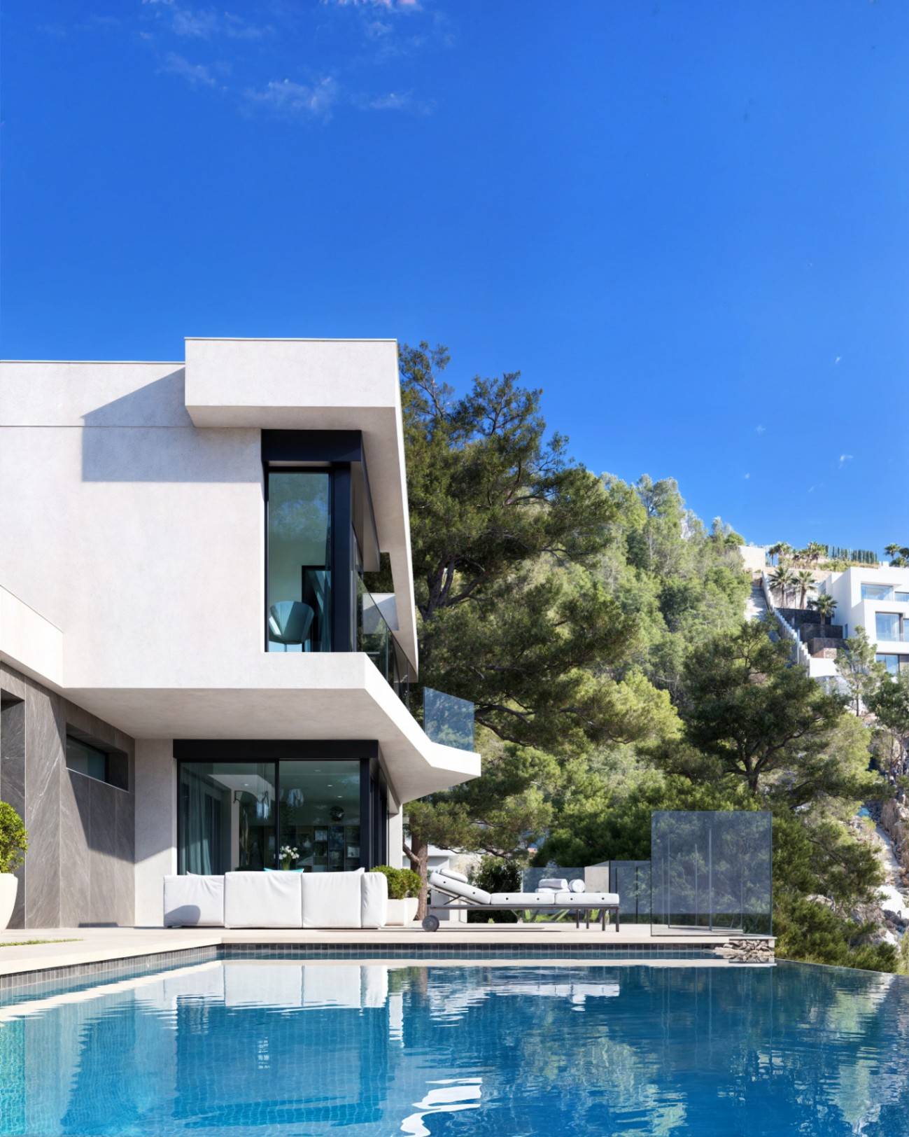 Fachada moderna con voladizos blancos, piscina infinity y terraza con mobiliario de diseño integrada en un entorno de pinos mediterráneos.