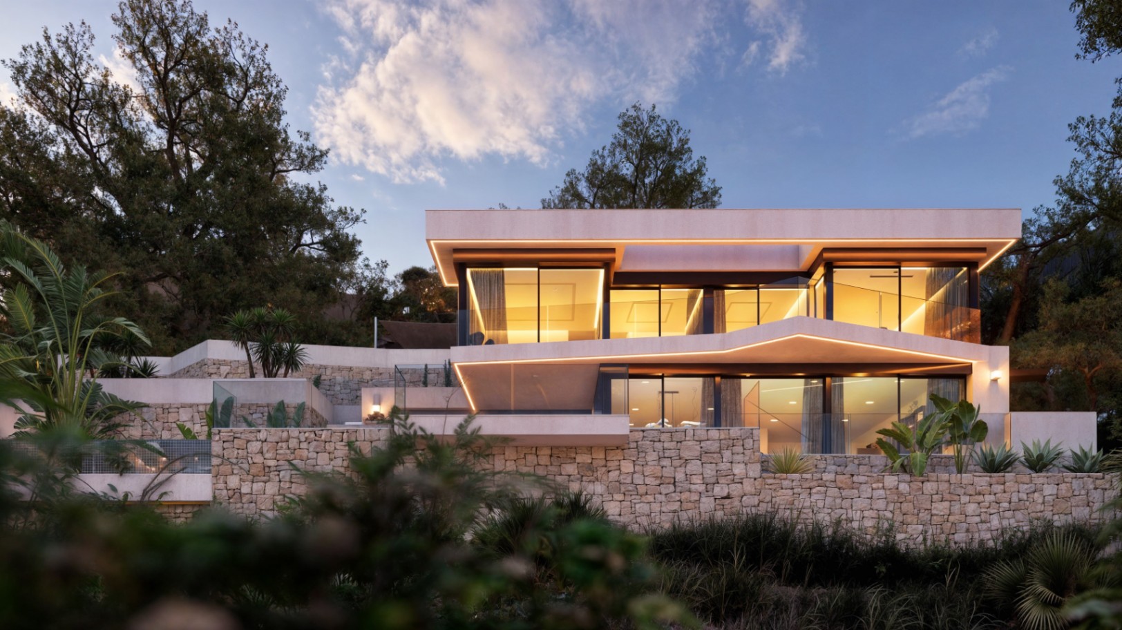 Fachada moderna de dos niveles con muros de piedra natural, amplios ventanales e iluminación LED integrada que resalta las líneas arquitectónicas al atardecer.