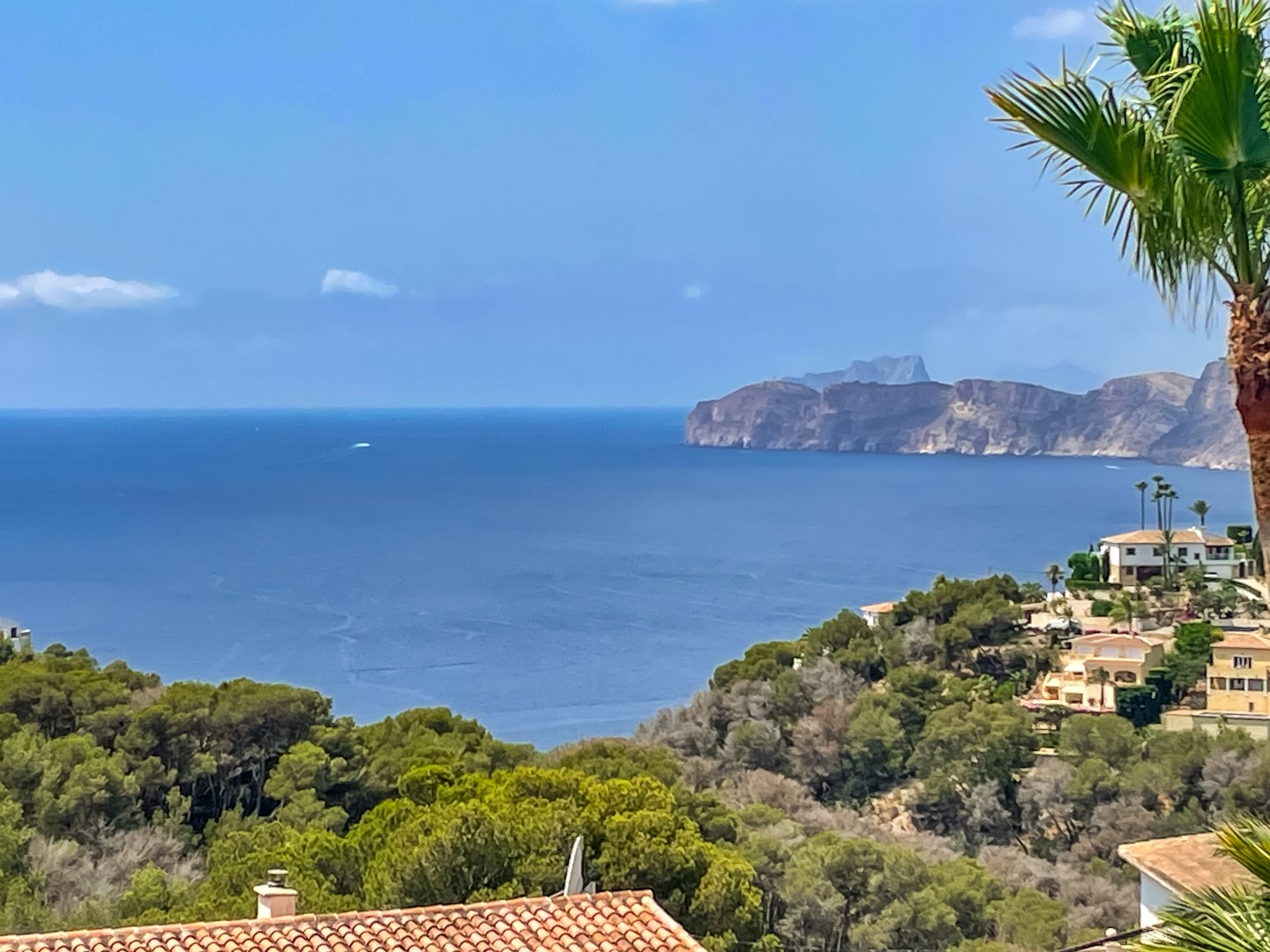 Vistas panorámicas hacia el mar Mediterráneo y los acantilados de Jávea, con un entorno natural de pinos y tejados tradicionales de terracota.