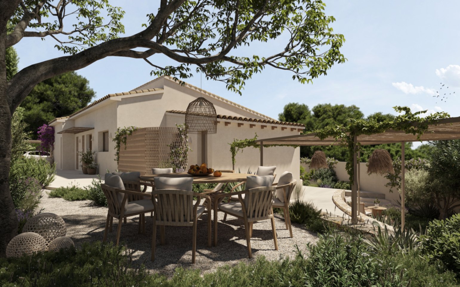 Comedor exterior sobre grava con mesa circular de madera, rodeado de vegetación autóctona y una pérgola de vigas naturales junto a la fachada de tonos cálidos.