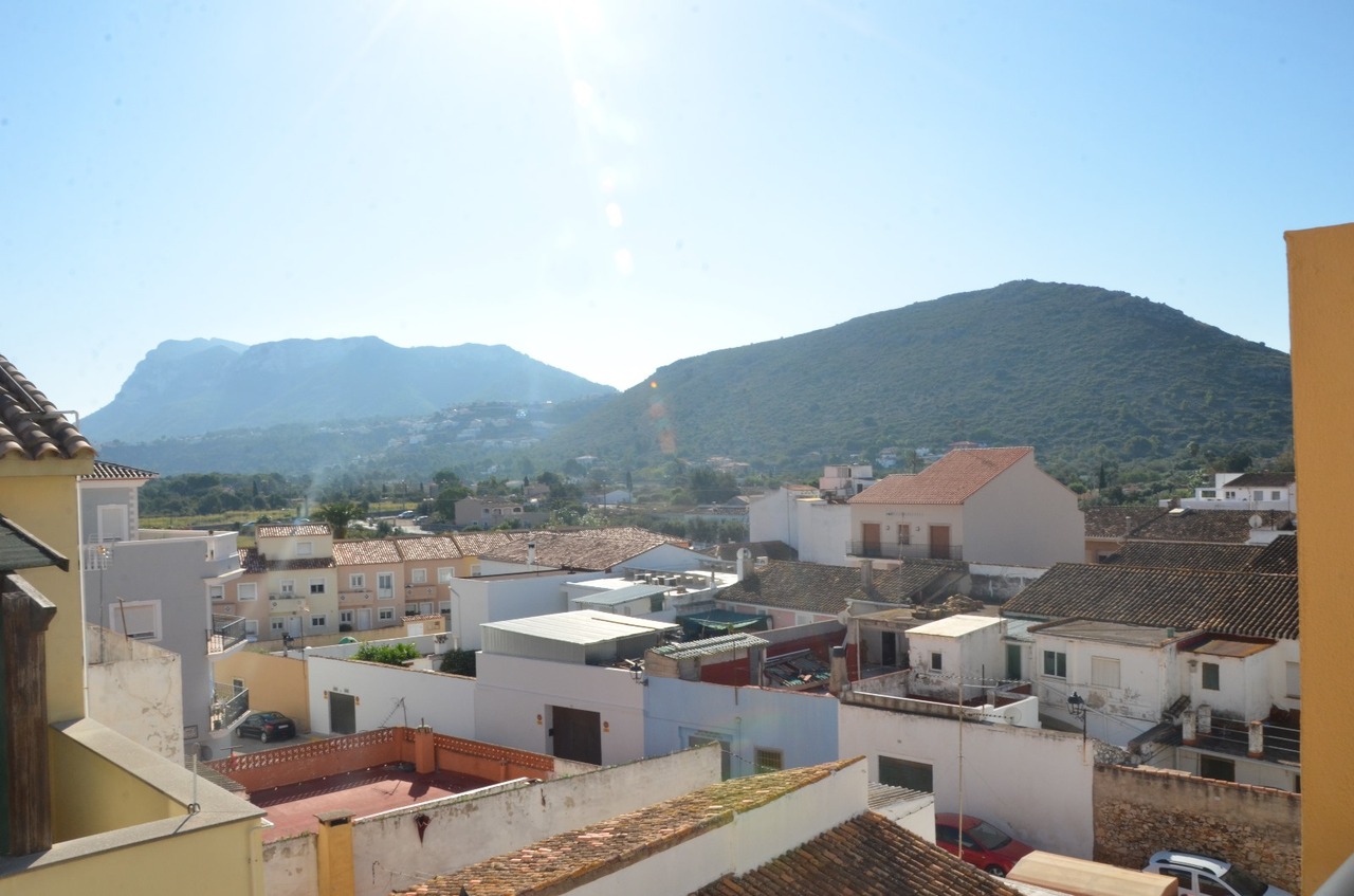 Vistas panorámicas elevadas sobre los tejados tradicionales del pueblo y las montañas circundantes bajo un cielo despejado y luminoso.