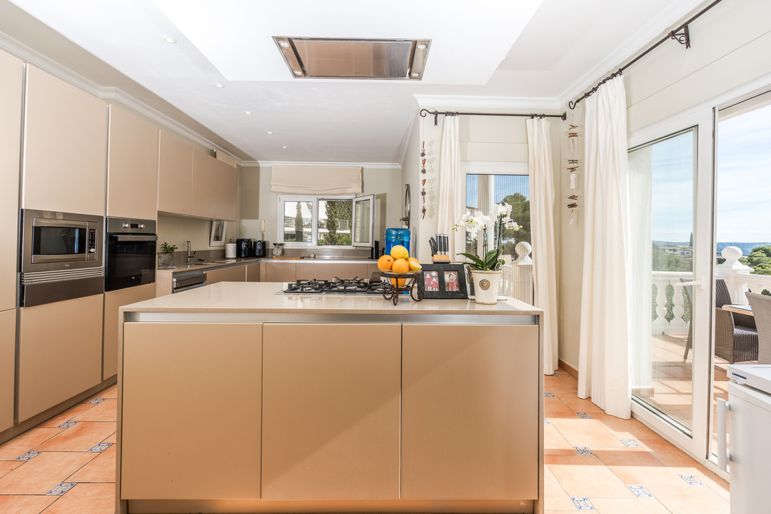 Cocina contemporánea con isla central, encimera de tono neutro y electrodomésticos integrados. El suelo de terracota y el acceso a la terraza aportan luminosidad.