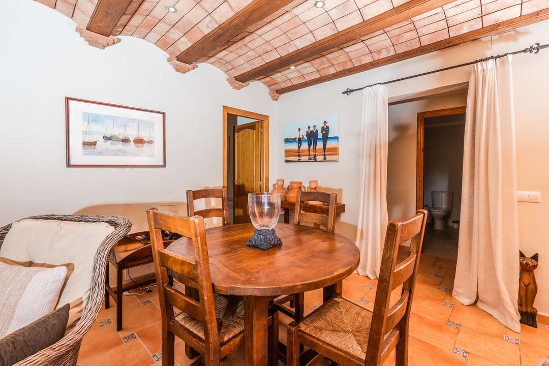 Comedor con techo de bóveda catalana y vigas de madera, suelo de terracota con detalles decorativos y mobiliario rústico de madera maciza.