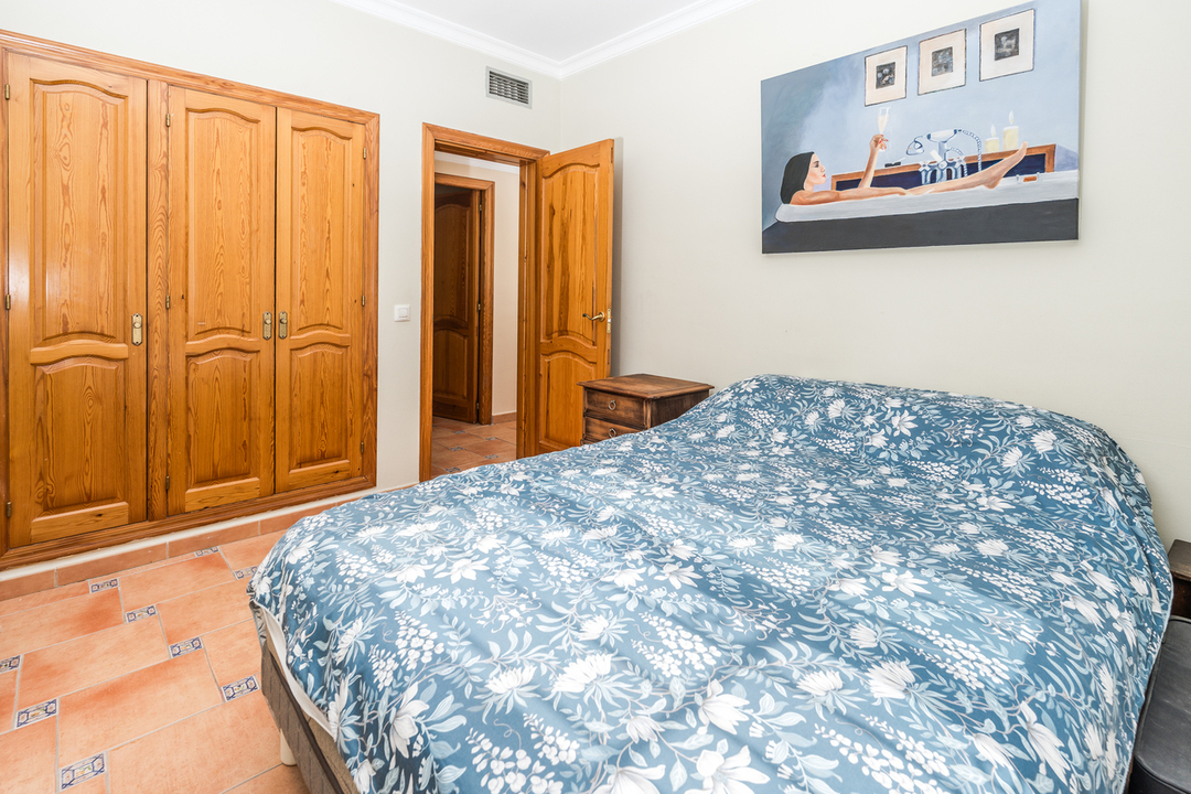 Dormitorio con armario empotrado de madera natural, suelos de terracota con detalles cerámicos y cama doble con textiles florales.