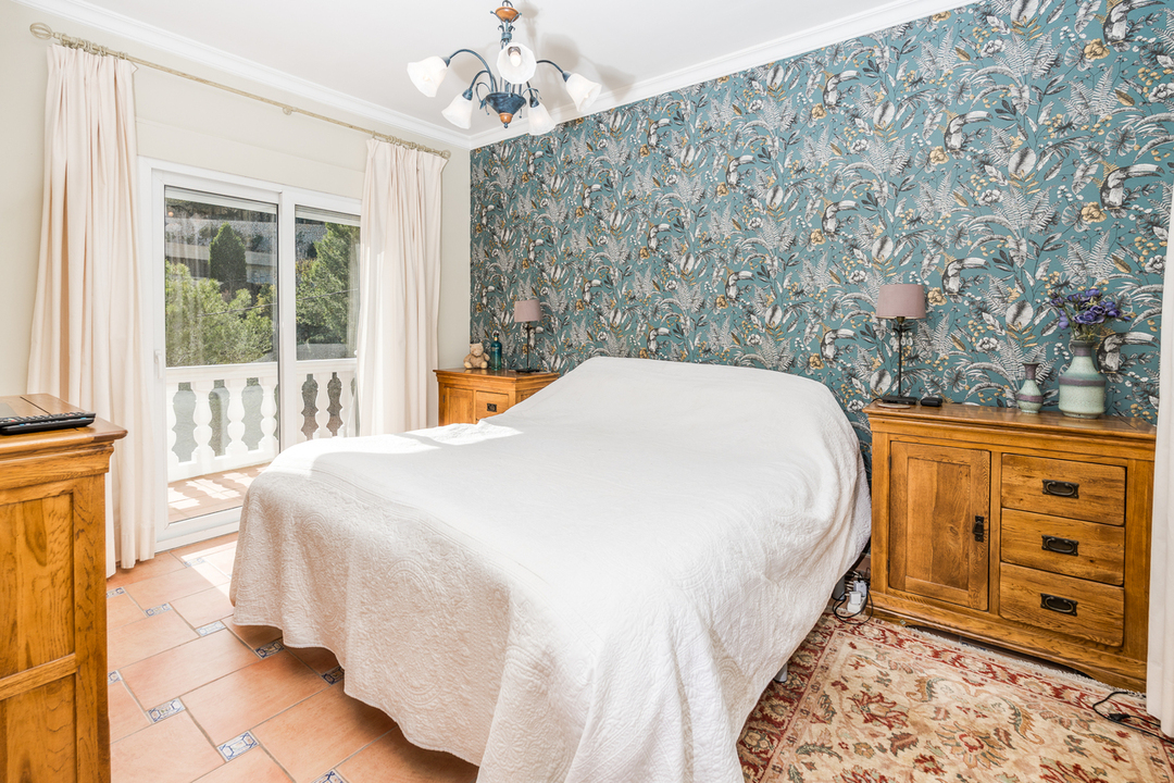 Dormitorio con papel pintado botánico, muebles de madera maciza y suelo de terracota. Incluye acceso directo a un balcón mediante puertas correderas.