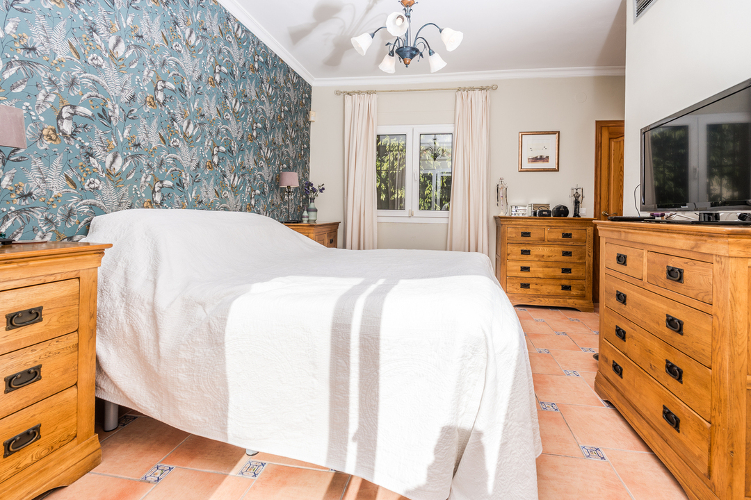 Dormitorio con pared de papel pintado tropical, mobiliario de madera clásica y suelos de terracota con detalles cerámicos.