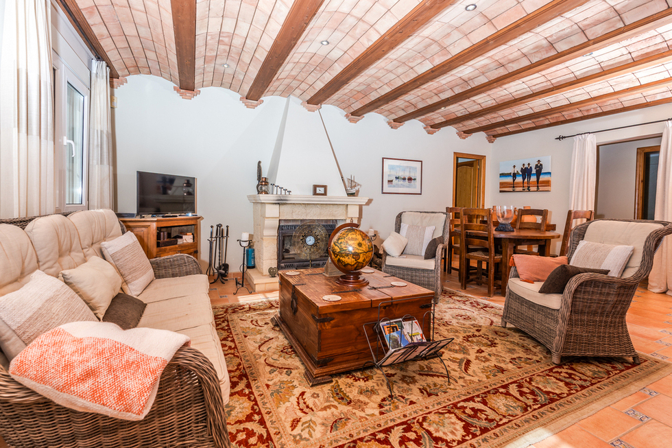 Salón con techo de bóveda catalana y vigas de madera, chimenea de piedra natural y mobiliario de mimbre sobre suelos de terracota.