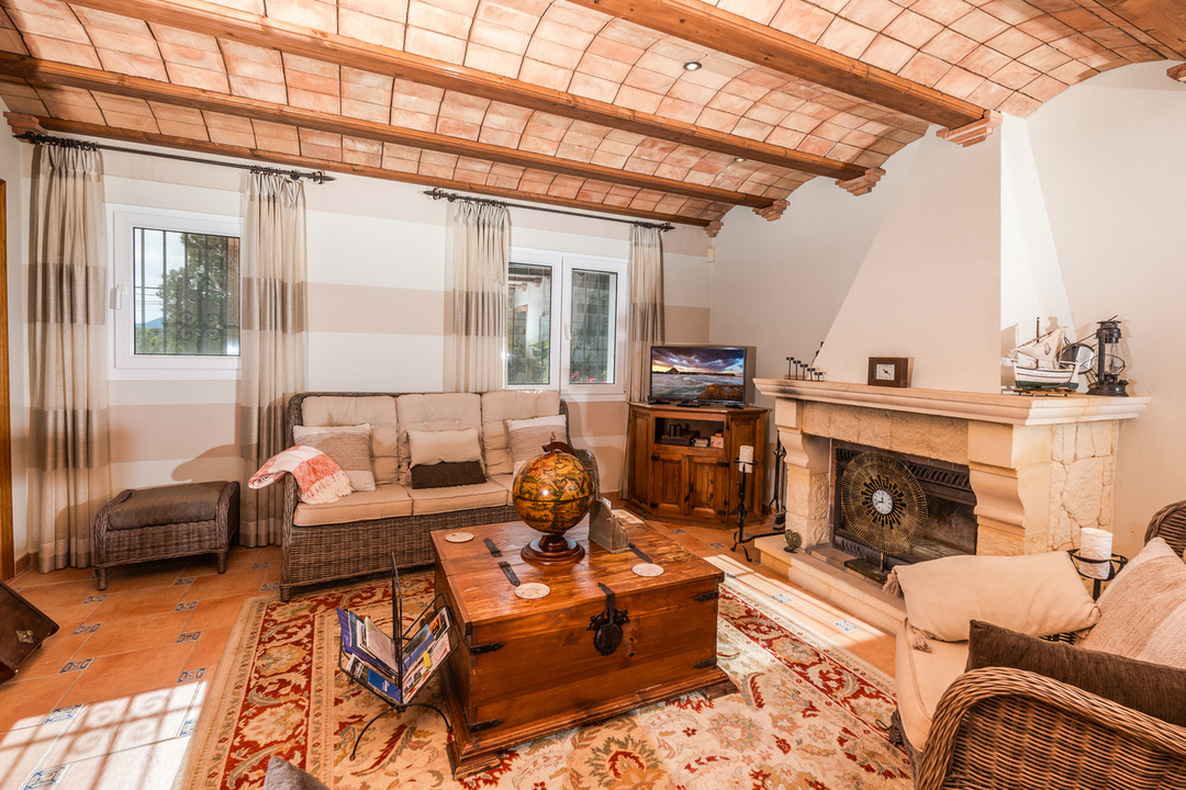 Salón con techo de bóveda catalana y vigas de madera, chimenea de piedra tallada y suelos de terracota con detalles cerámicos tradicionales.