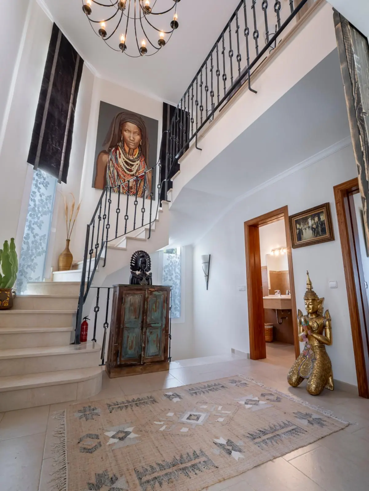 Entrada principal con escalera de mármol y barandilla de hierro, decorada con un gran retrato, una estatua budista dorada y una alfombra de estilo étnico.
