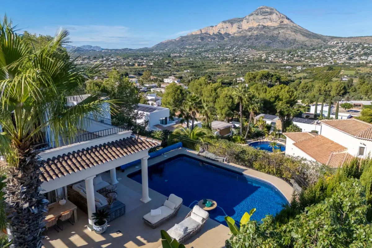 Vista elevada de la piscina privada y porche con columnas blancas, ofreciendo vistas panorámicas al valle y al macizo del Montgó bajo un cielo despejado.