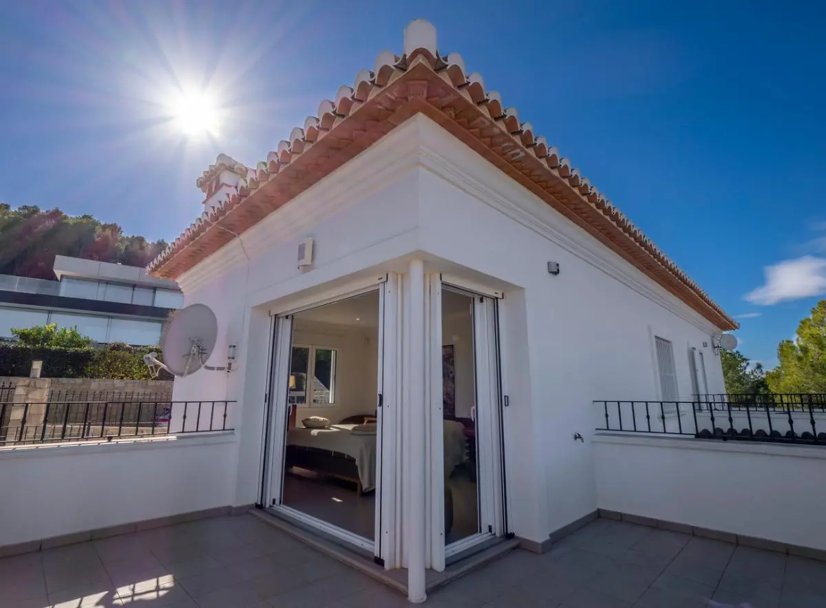Vista exterior de un dormitorio en planta superior con puertas correderas de cristal que dan acceso a una terraza privada bajo un tejado de teja tradicional.