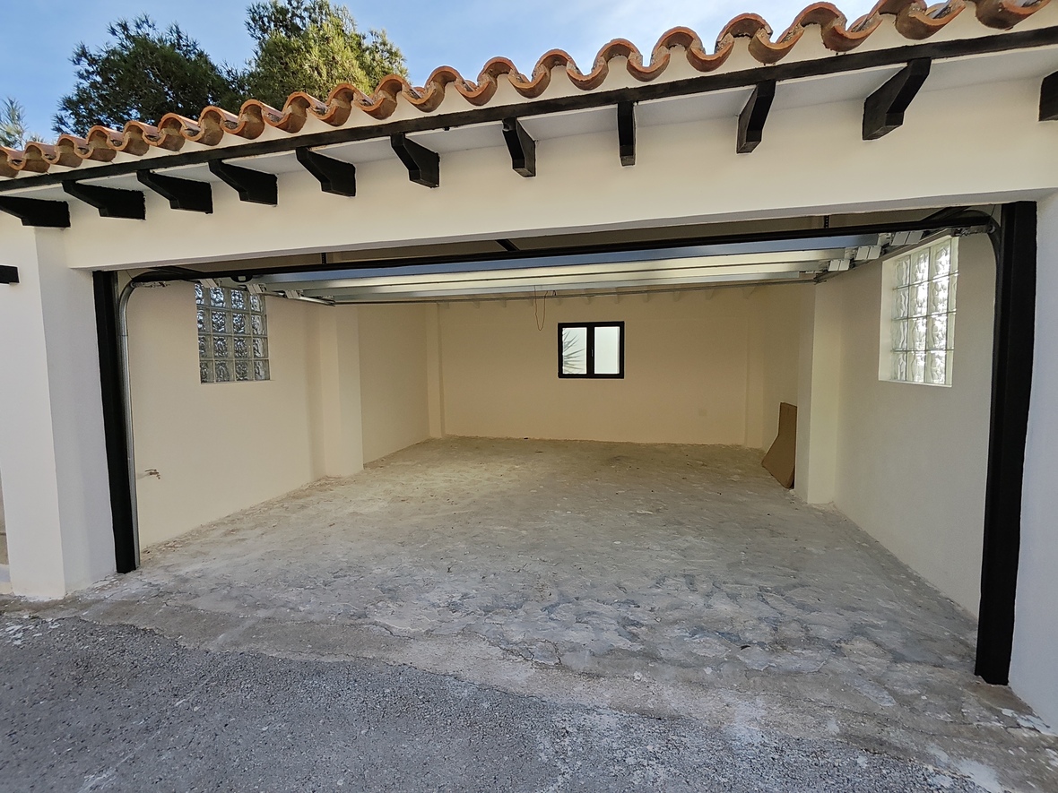 Amplio garaje con suelo de hormigón, ventanas laterales de bloques de vidrio y techado tradicional de tejas con vigas de madera oscura.
