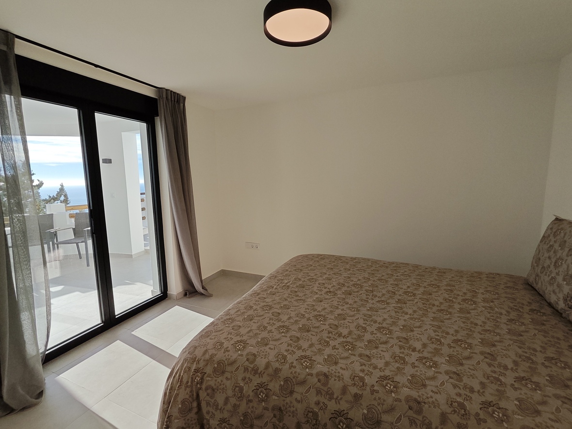 Dormitorio con cama doble, textiles florales y acceso directo a una terraza privada con vistas al mar a través de puertas correderas acristaladas.