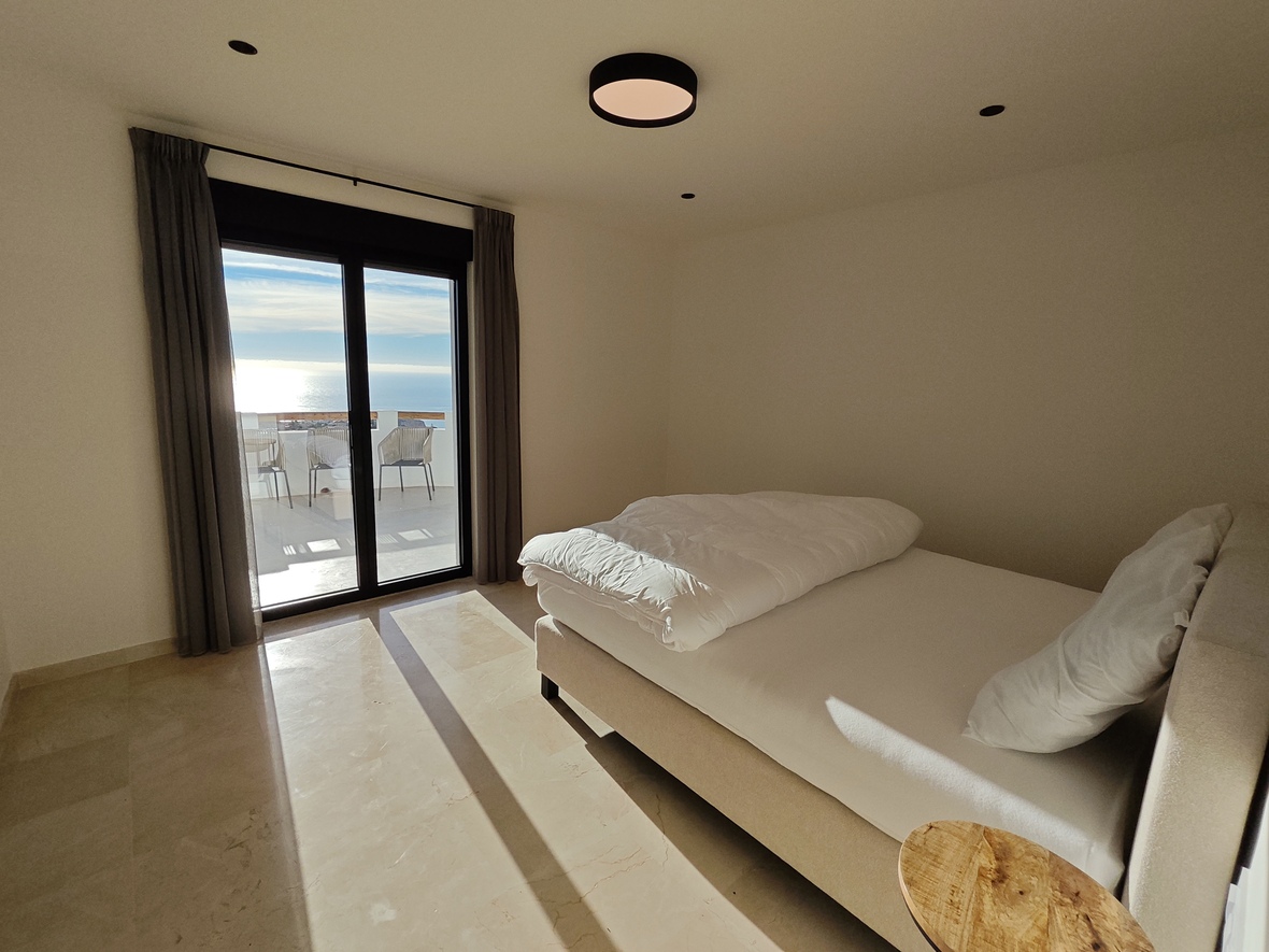 Dormitorio contemporáneo con suelos de mármol pulido, cama doble y acceso directo a una terraza con vistas panorámicas al mar.