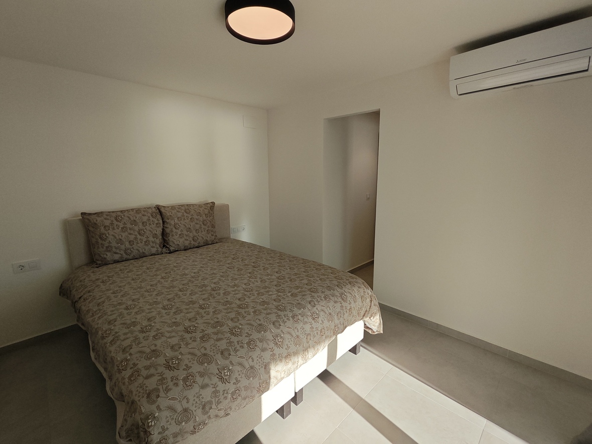 Dormitorio de diseño sobrio con cama doble, textiles estampados, aire acondicionado individual y suelos de gres en tonos claros.