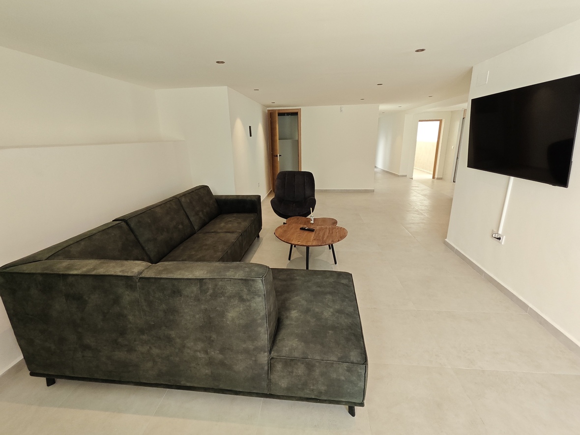 Sala de estar moderna con sofá rinconera verde oscuro, mesa de centro de madera y televisor de pantalla plana montado en pared con suelos cerámicos claros.