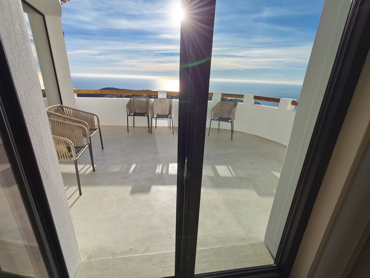 Terraza con vistas panorámicas al mar, equipada con sillas de cuerda trenzada, paredes blancas con pasamanos de madera y suelo de hormigón pulido.