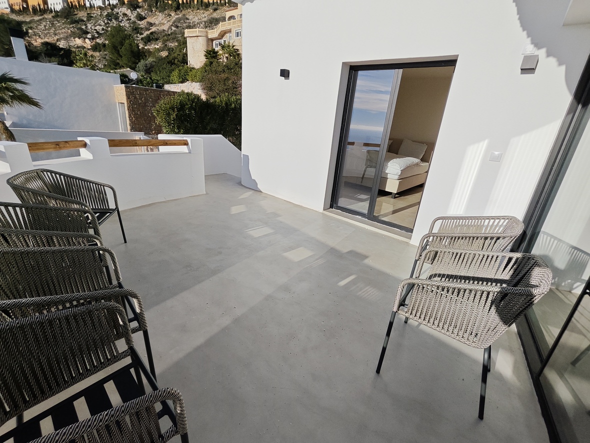 Terraza de microcemento con sillas de diseño en cuerda trenzada y acceso directo al dormitorio a través de amplios ventanales correderos.