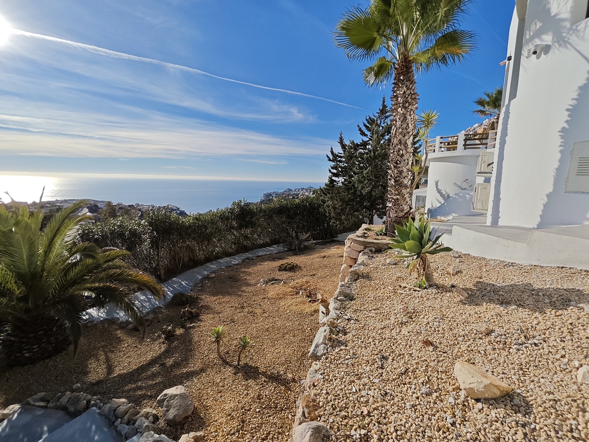 Terraza elevada con jardín de grava, palmeras y plantas suculentas, ofreciendo vistas panorámicas al mar Mediterráneo y la costa circundante.