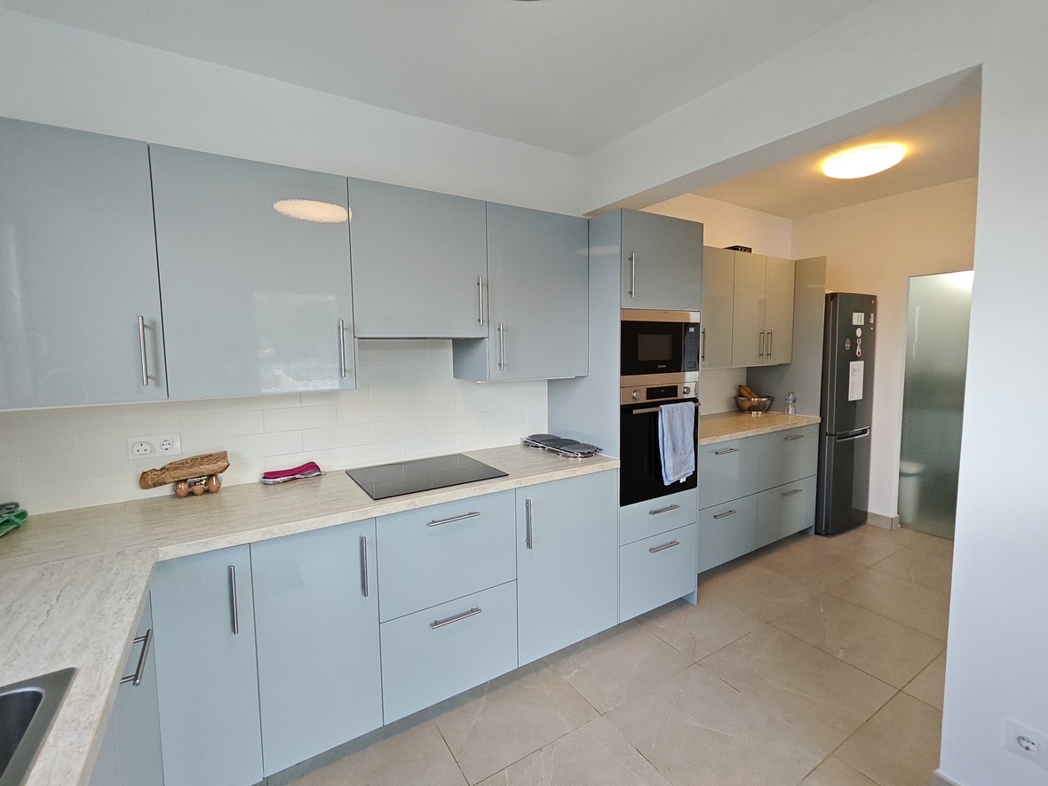 Cocina moderna con armarios en azul pálido brillante, encimera de efecto piedra clara y electrodomésticos integrados sobre un suelo de gres porcelánico.