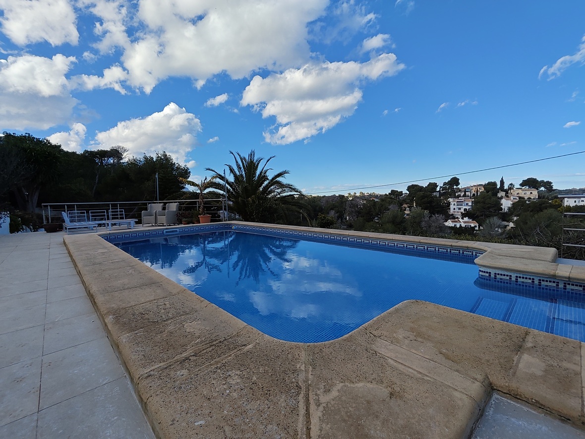 Piscina exterior con revestimiento de gresite azul y bordes de piedra, ofreciendo vistas despejadas al entorno natural y residencial circundante.