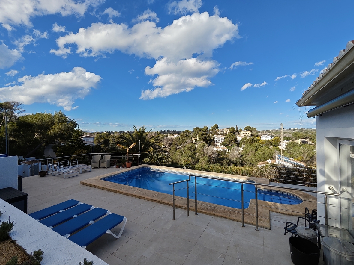 Terraza elevada con piscina rectangular, barandillas de acero inoxidable y vistas despejadas al entorno natural mediterráneo y urbanizaciones.