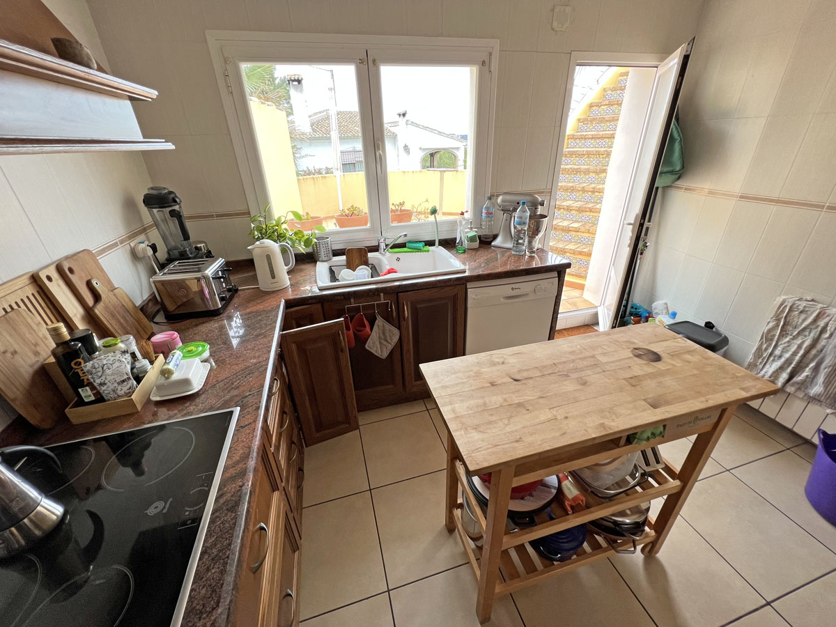 Cocina independiente con encimeras de granito, armarios de madera y una isla auxiliar móvil. Incluye acceso directo a una escalera exterior con azulejos tradicionales.