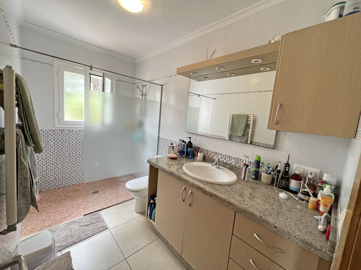 Cuarto de baño con encimera de granito, mueble de madera y espejo con focos. Incluye una amplia zona de ducha con mampara de cristal translúcido y ventana exterior.