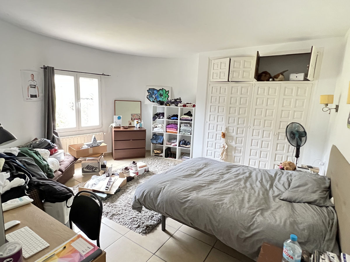 Dormitorio con amplio armario empotrado de puertas blancas paneladas, ventanal con luz natural y suelos cerámicos. Dispone de espacio para zona de trabajo y almacenaje.