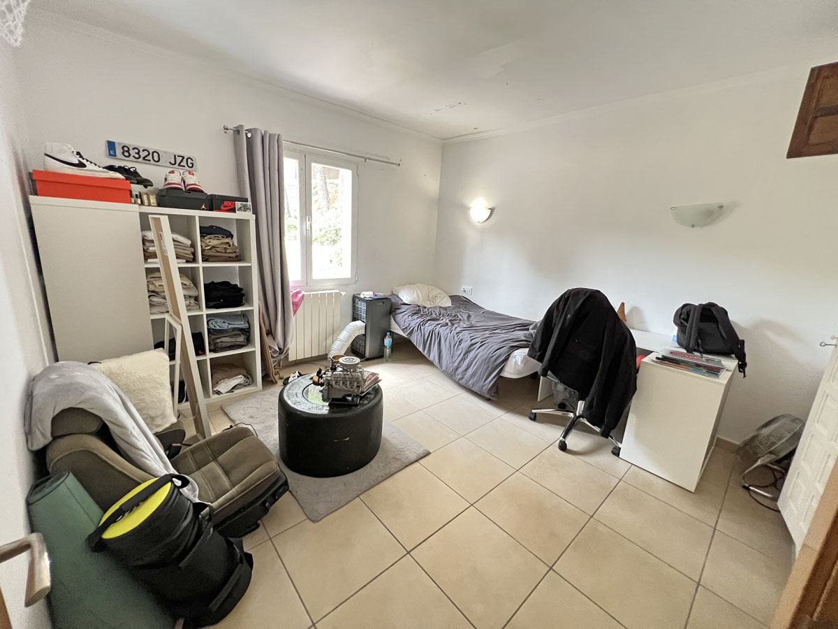 Dormitorio del estudio independiente con suelos de gres, paredes blancas y luz natural. El espacio incluye zona para escritorio y estanterías de almacenaje.