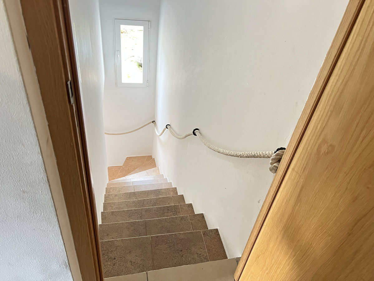 Escalera interior con peldaños cerámicos y un original pasamanos de cuerda, que conecta los niveles de la vivienda bajo luz natural.