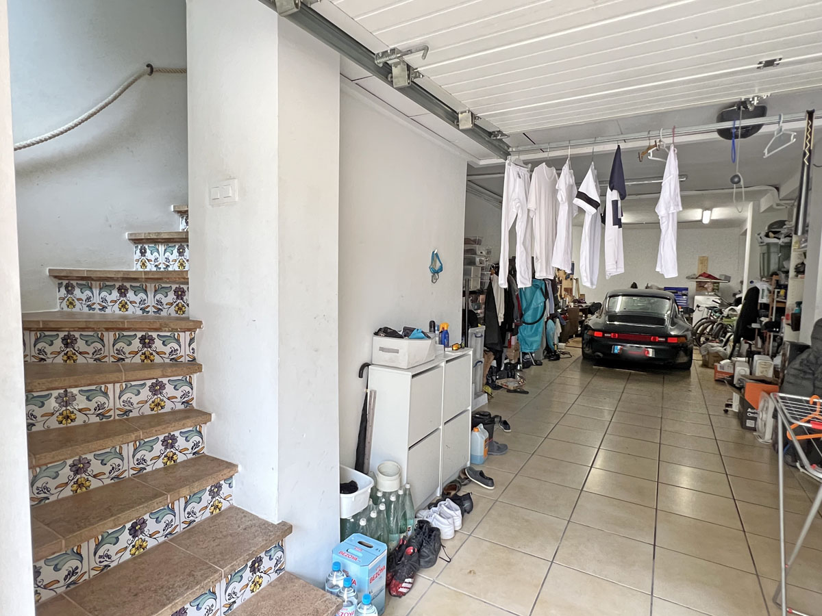 Garaje espacioso con suelos cerámicos y acceso directo a la vivienda mediante una escalera decorada con azulejos tradicionales mediterráneos.