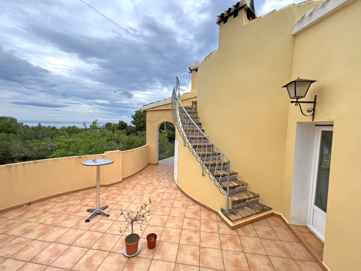 Terraza exterior con suelo de gres cerámico, escalera curva con azulejos decorativos y vistas panorámicas al mar Mediterráneo y al entorno natural.