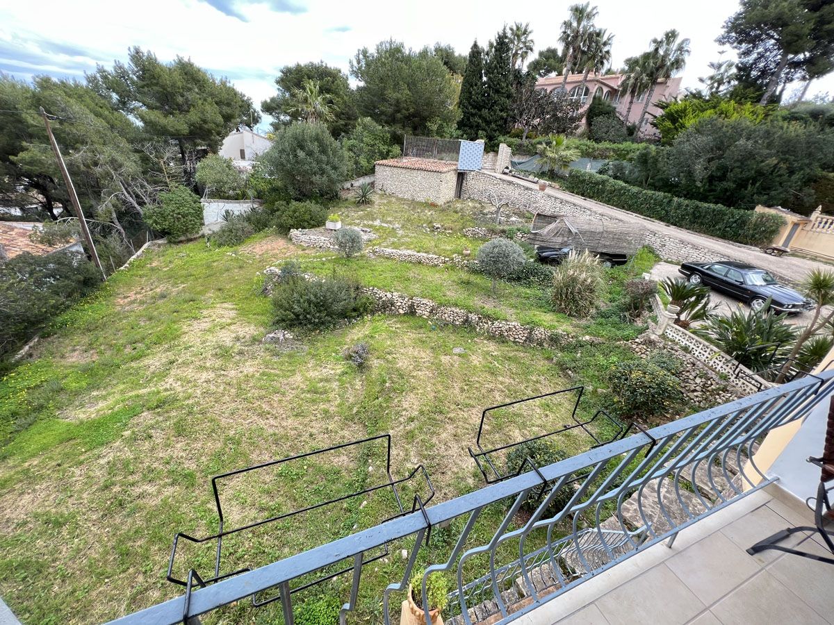 Vista desde la terraza superior hacia la amplia parcela aterrazada con muros de piedra natural, rodeada de vegetación mediterránea y pinos.