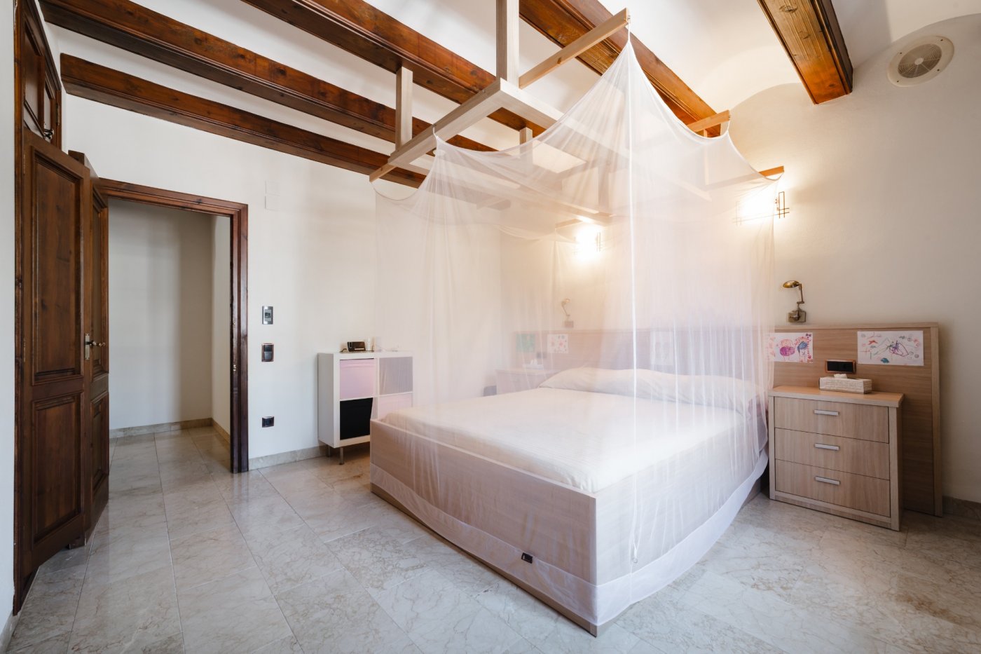 Dormitorio con vigas de madera vista, suelos de mármol y cama doble equipada con una estructura de madera para mosquitera integrada en el techo.