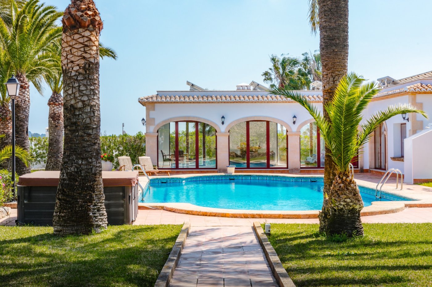 Piscina de 16x7 metros rodeada de palmeras maduras, con vistas a la casa de invitados de estilo mediterráneo y arcos de piedra tosca bajo paneles solares.