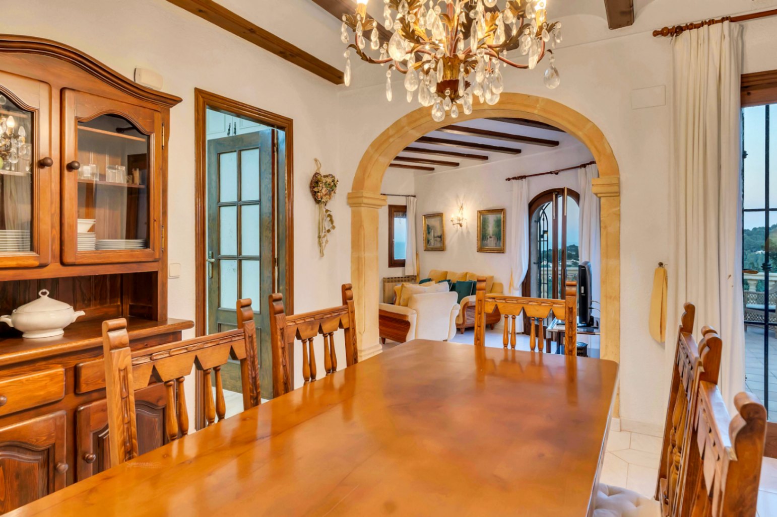 Comedor con mobiliario de madera maciza, vigas vistas y un arco de piedra tosca que comunica con el salón y la terraza con vistas.