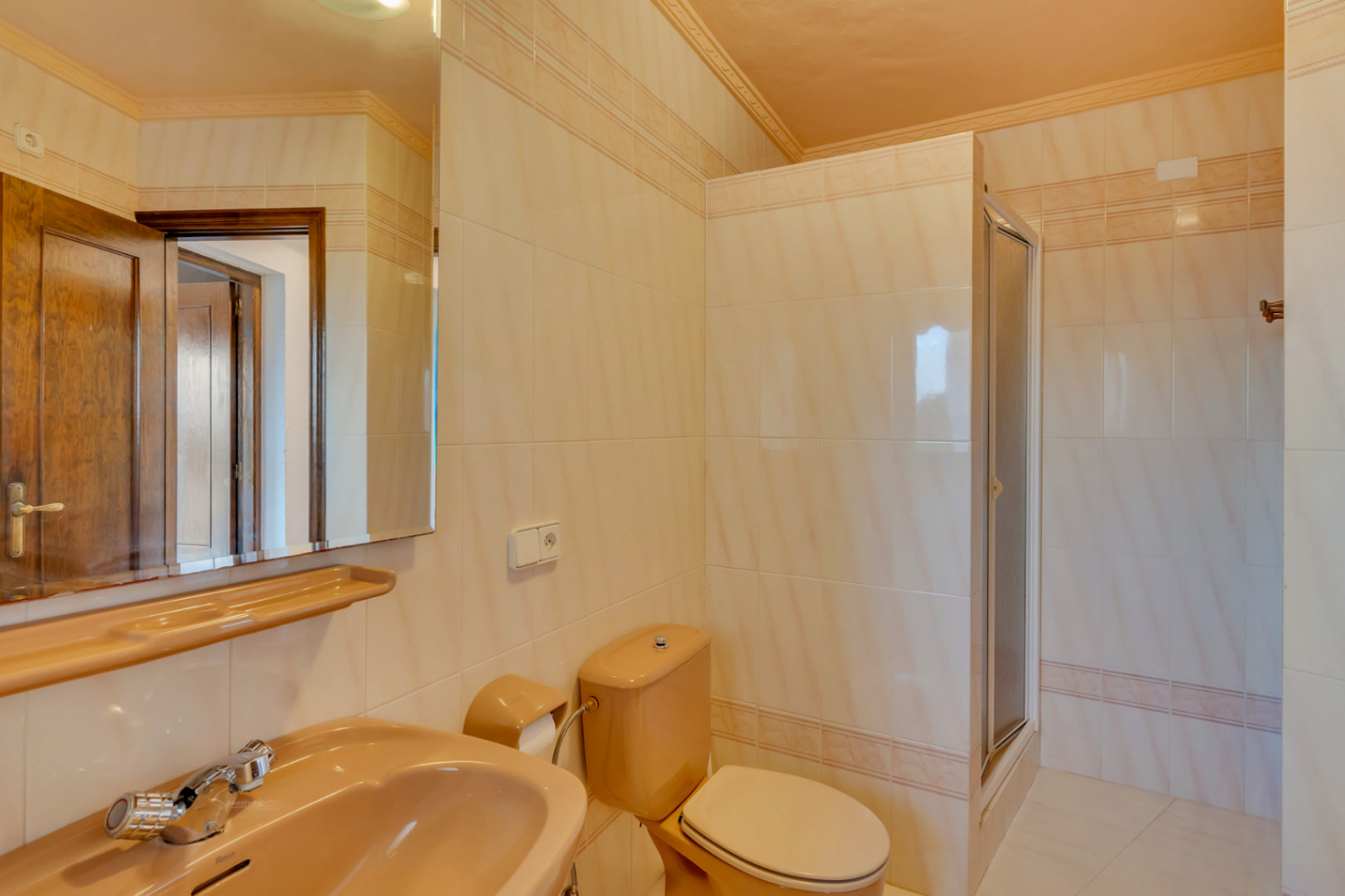 Cuarto de baño con azulejos beige y cenefa decorativa, equipado con sanitarios en tono melocotón, espejo de gran formato y plato de ducha con mampara.