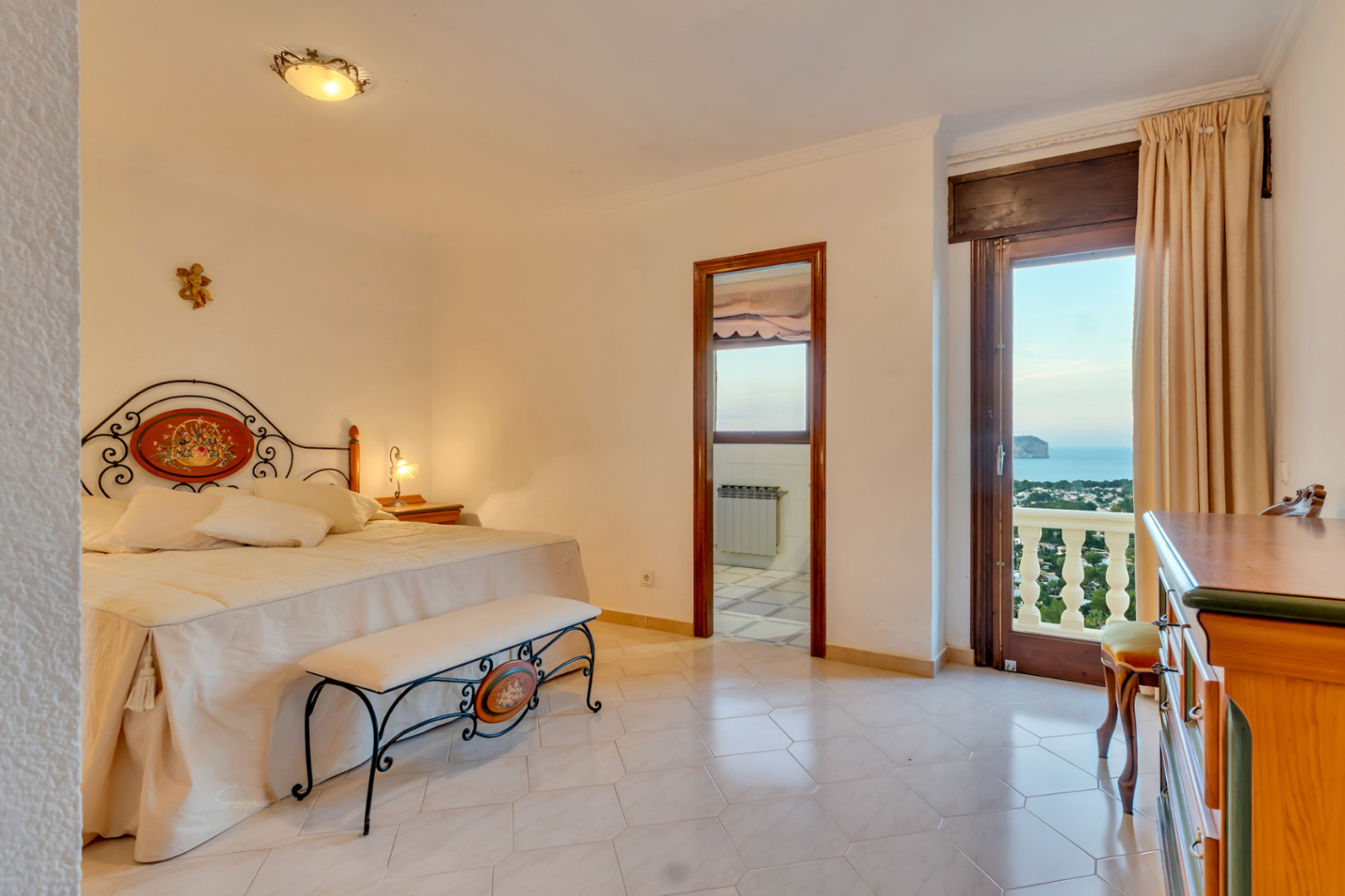 Dormitorio principal con cama de forja, suelo cerámico y acceso directo a terraza con vistas al mar y al Cabo San Antonio. Incluye baño en suite visible.