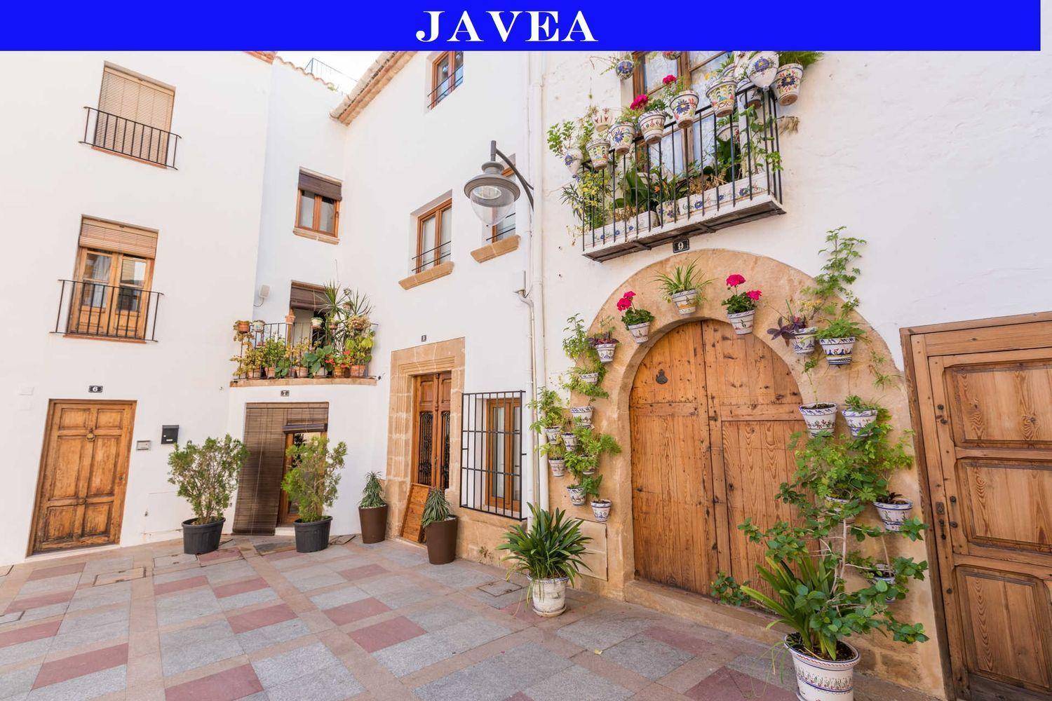 Fachada tradicional en el casco antiguo de Jávea con muros blancos, puertas de madera y arcos de piedra tosca decorados con macetas de cerámica.