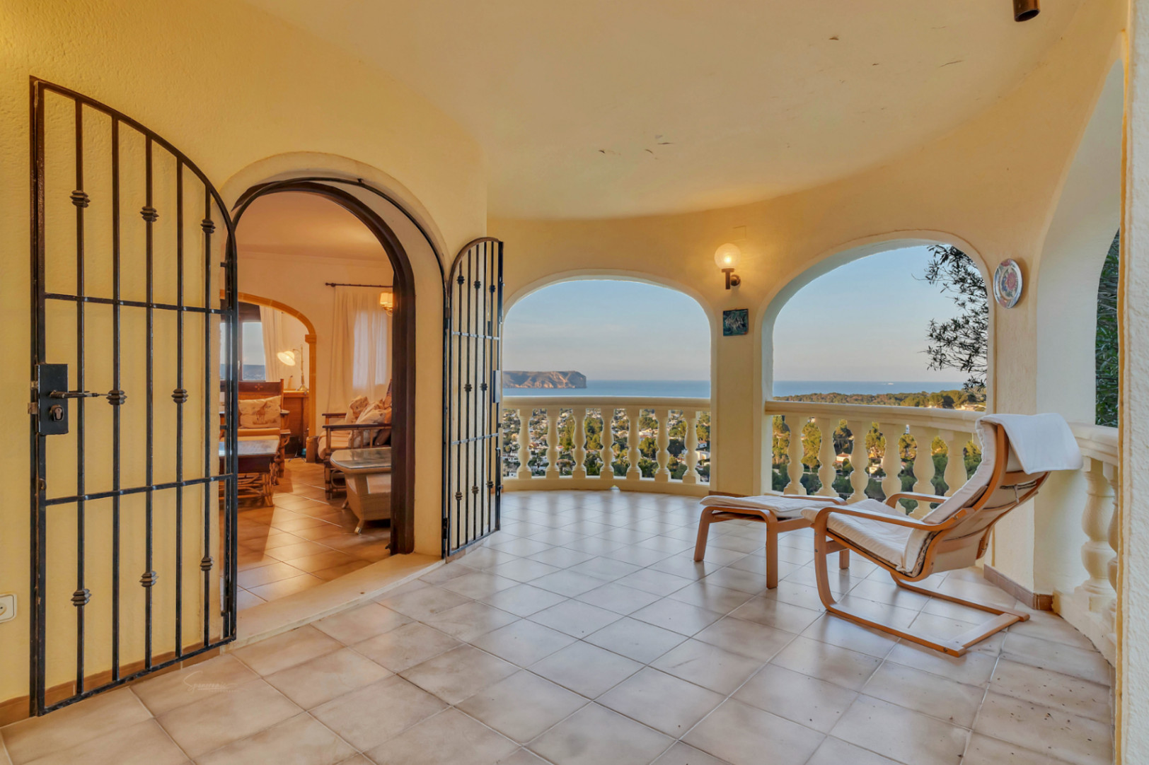Terraza cubierta con arcos de medio punto, balaustrada clásica y vistas panorámicas al Cabo San Antonio. Suelos cerámicos y acceso directo al salón mediante puerta de forja.