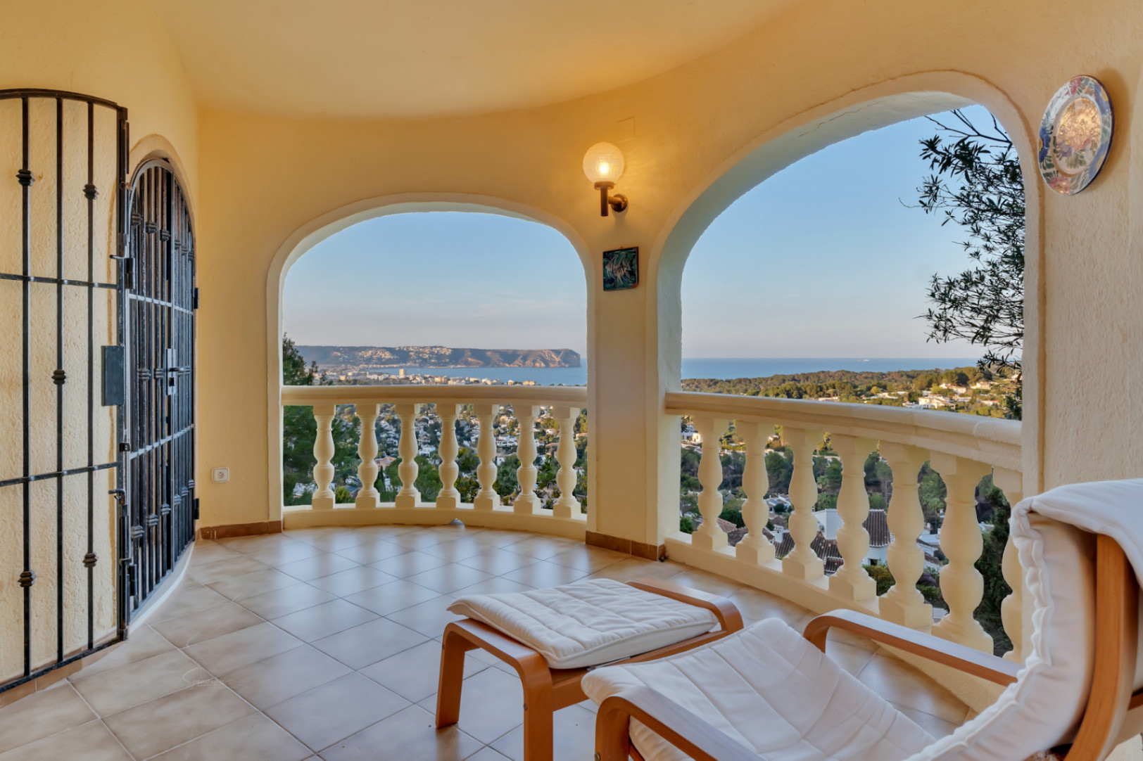 Terraza cubierta con arcos y balaustrada, ofreciendo vistas panorámicas a la bahía de Jávea y el Cabo San Antonio. Incluye mobiliario de descanso y suelos cerámicos.