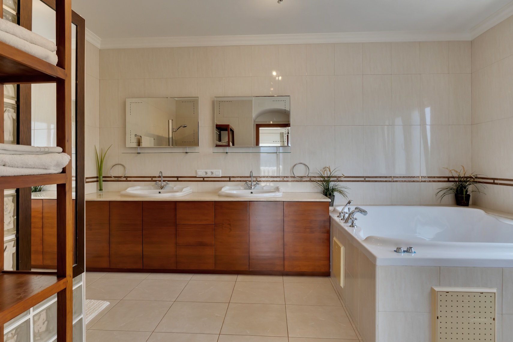 Baño principal con mueble de madera de doble lavabo, espejos individuales y una amplia bañera de hidromasaje integrada en gres porcelánico.