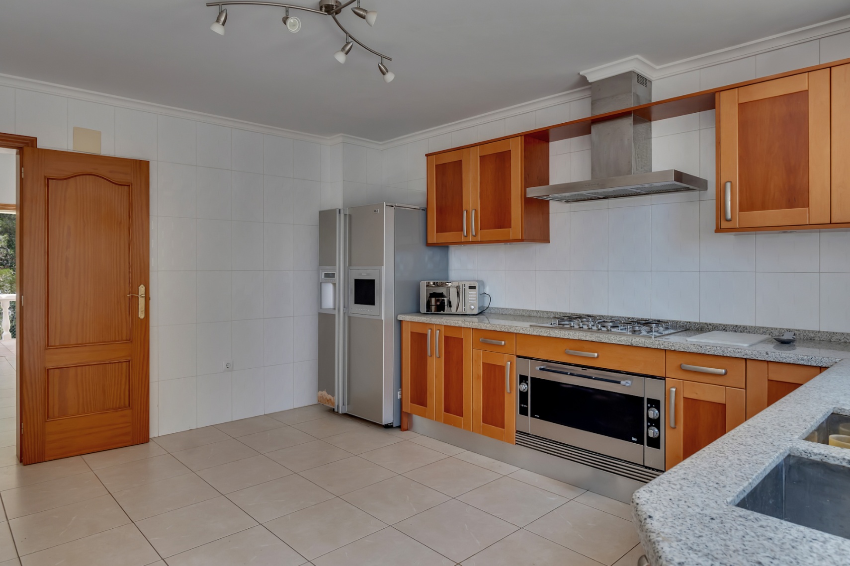Cocina equipada con armarios de madera, encimeras de granito gris y electrodomésticos de acero inoxidable, incluyendo un frigorífico americano y placa de gas.