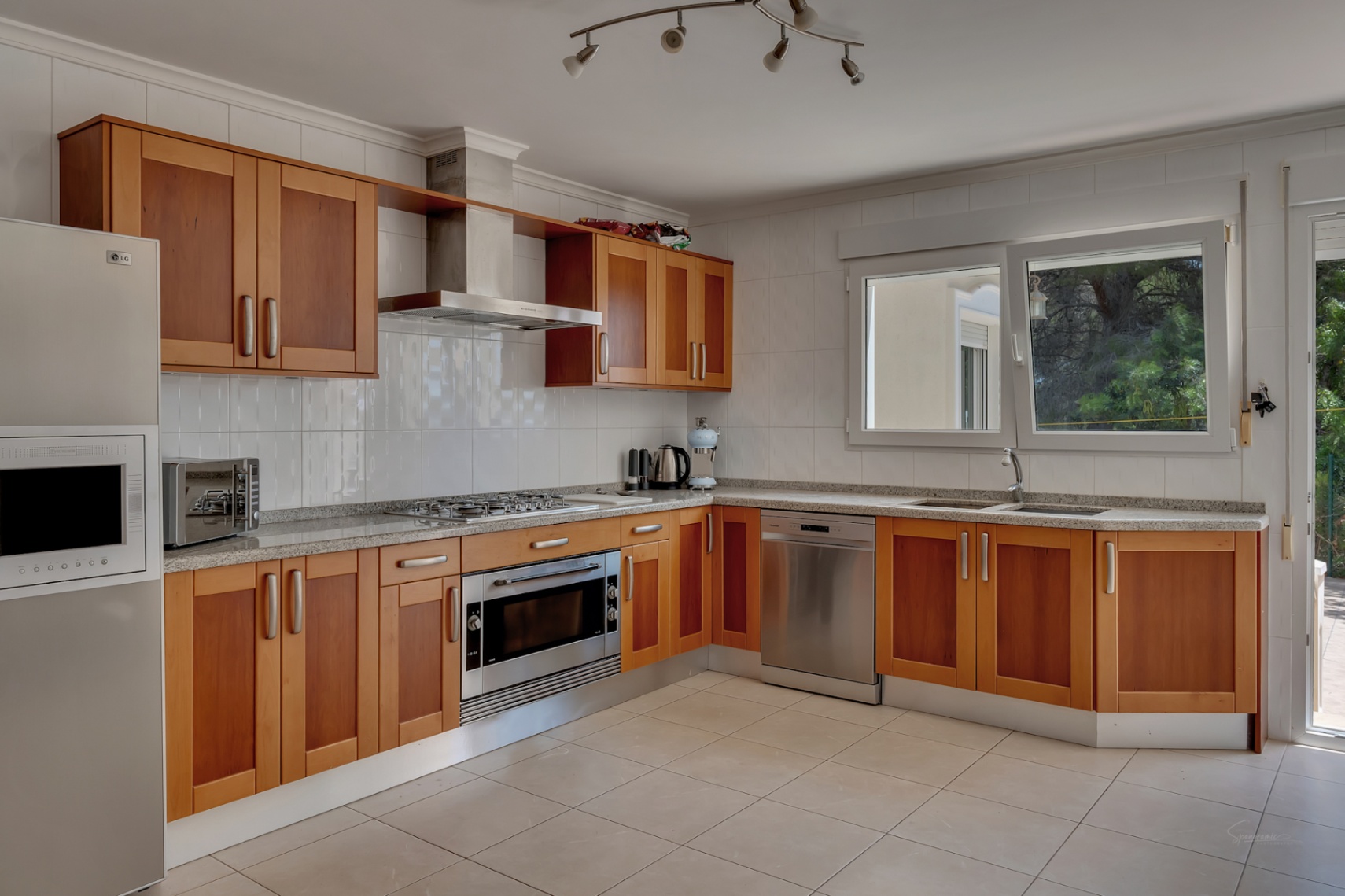 Cocina equipada con mobiliario de madera, encimera de granito, electrodomésticos de acero inoxidable y amplia ventana que aporta luz natural al espacio.