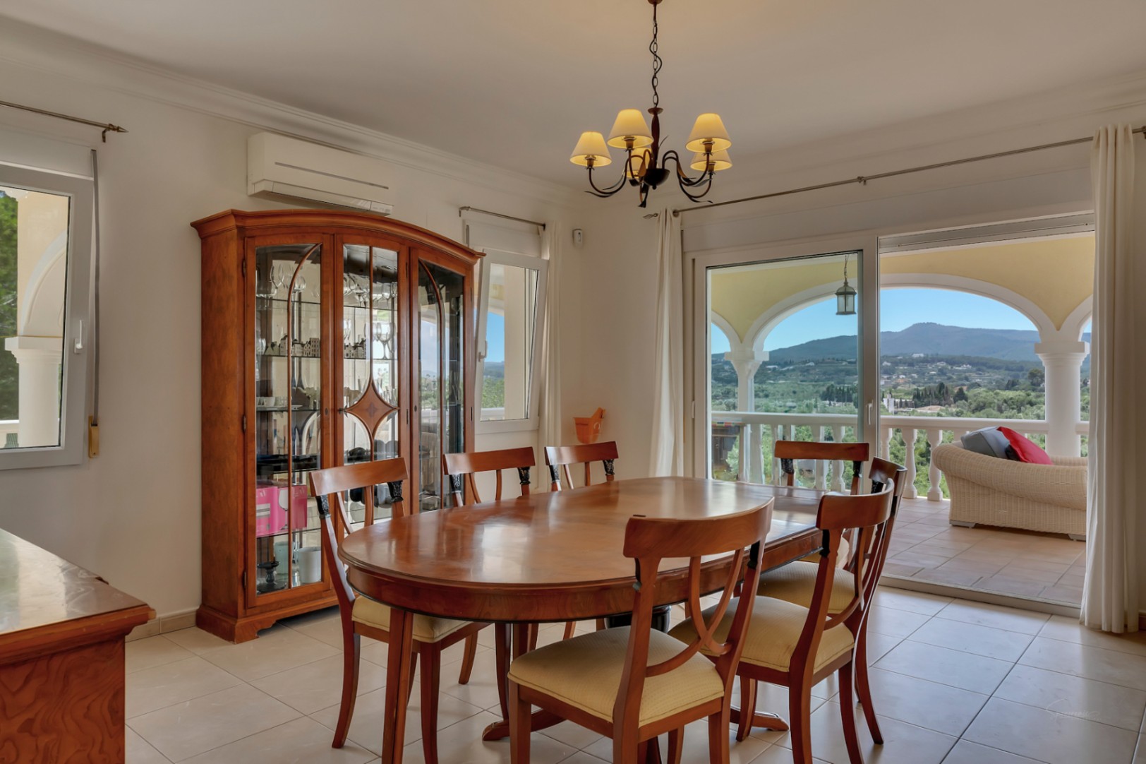 Comedor espacioso con mesa ovalada de madera, vitrina clásica y acceso directo a la naya con vistas panorámicas al valle y al Montgó.