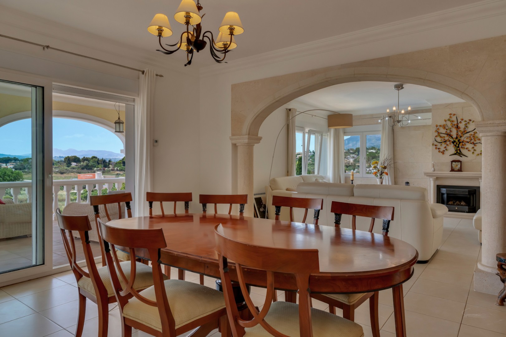 Comedor luminoso con mesa de madera noble, conectado al salón por un arco de piedra tosca y acceso directo a la naya con vistas panorámicas al valle.