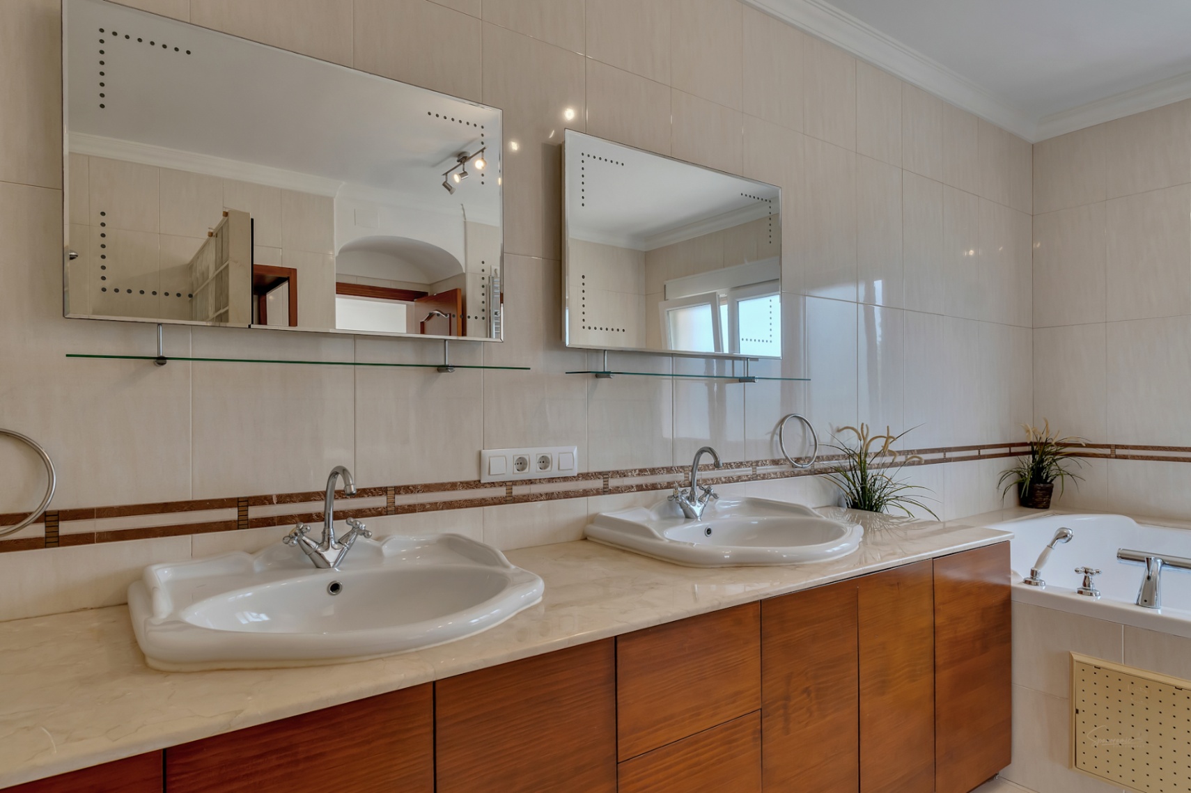 Cuarto de baño con doble lavabo sobre encimera de mármol, muebles de madera, espejos con iluminación integrada y bañera lateral.