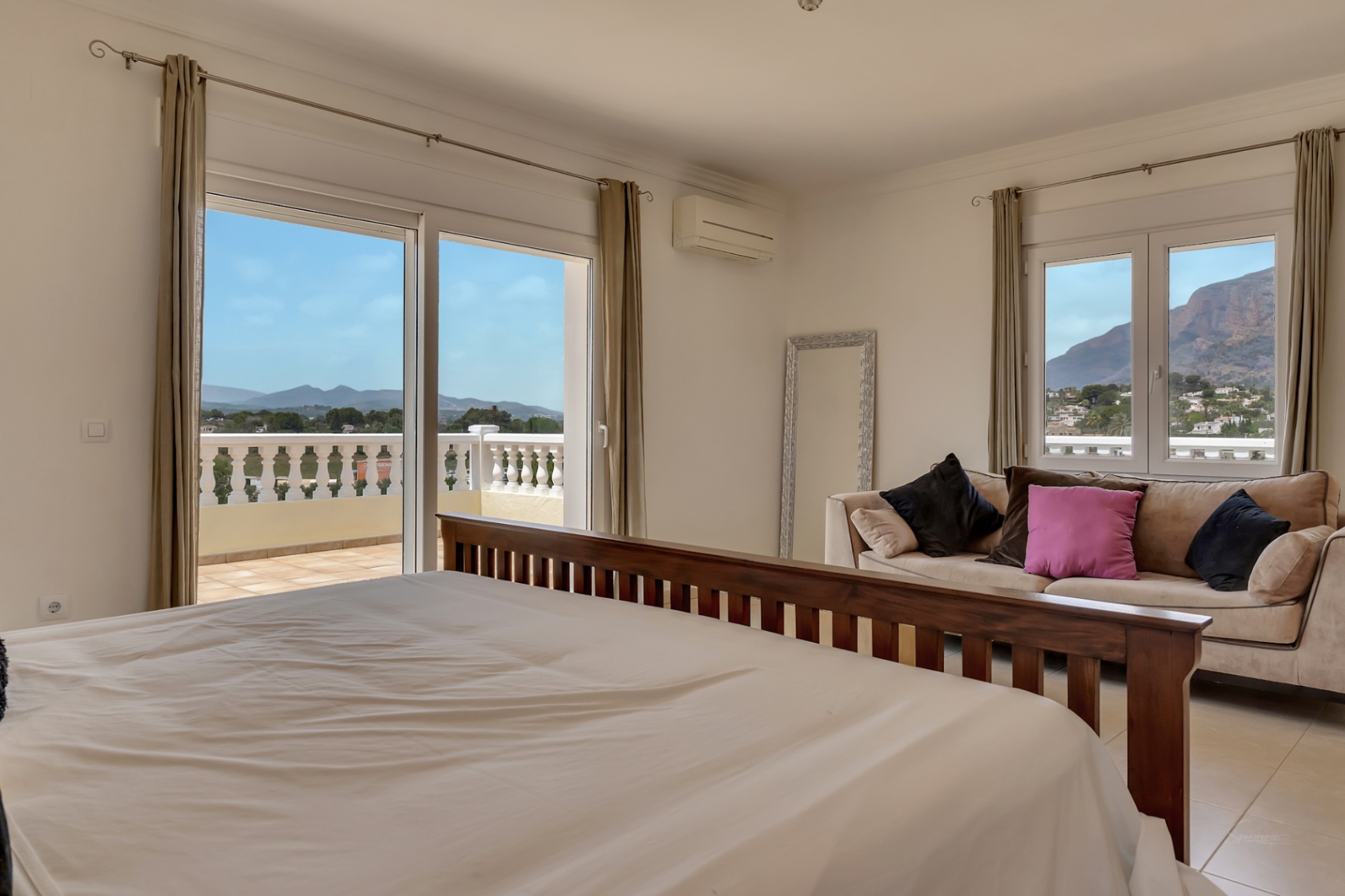 Dormitorio principal con cama de madera oscura, zona de estar y acceso directo a terraza con vistas al Montgó y balustrada clásica.